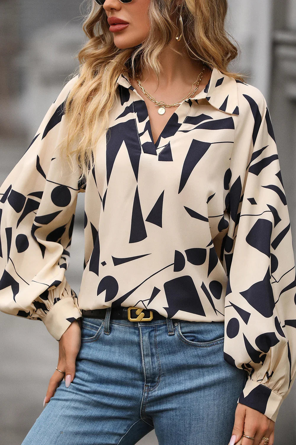 Woman wearing a beige abstract print blouse with balloon sleeves and blue jeans