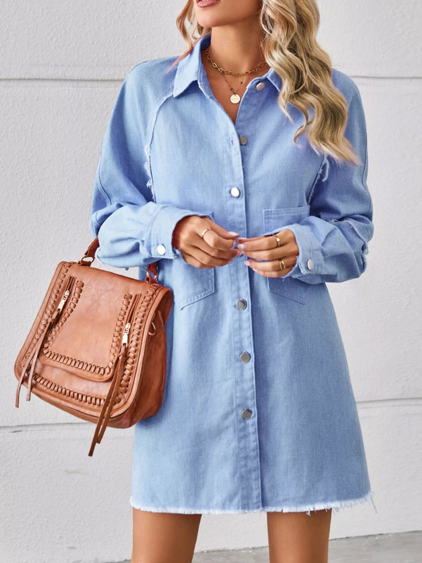 Woman wearing light blue denim shirt dress with tan handbag and layered necklaces
