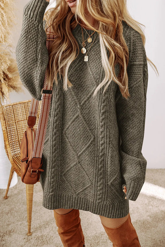 Woman wearing oversized gray cable knit sweater dress with layered gold necklaces and brown suede knee-high boots