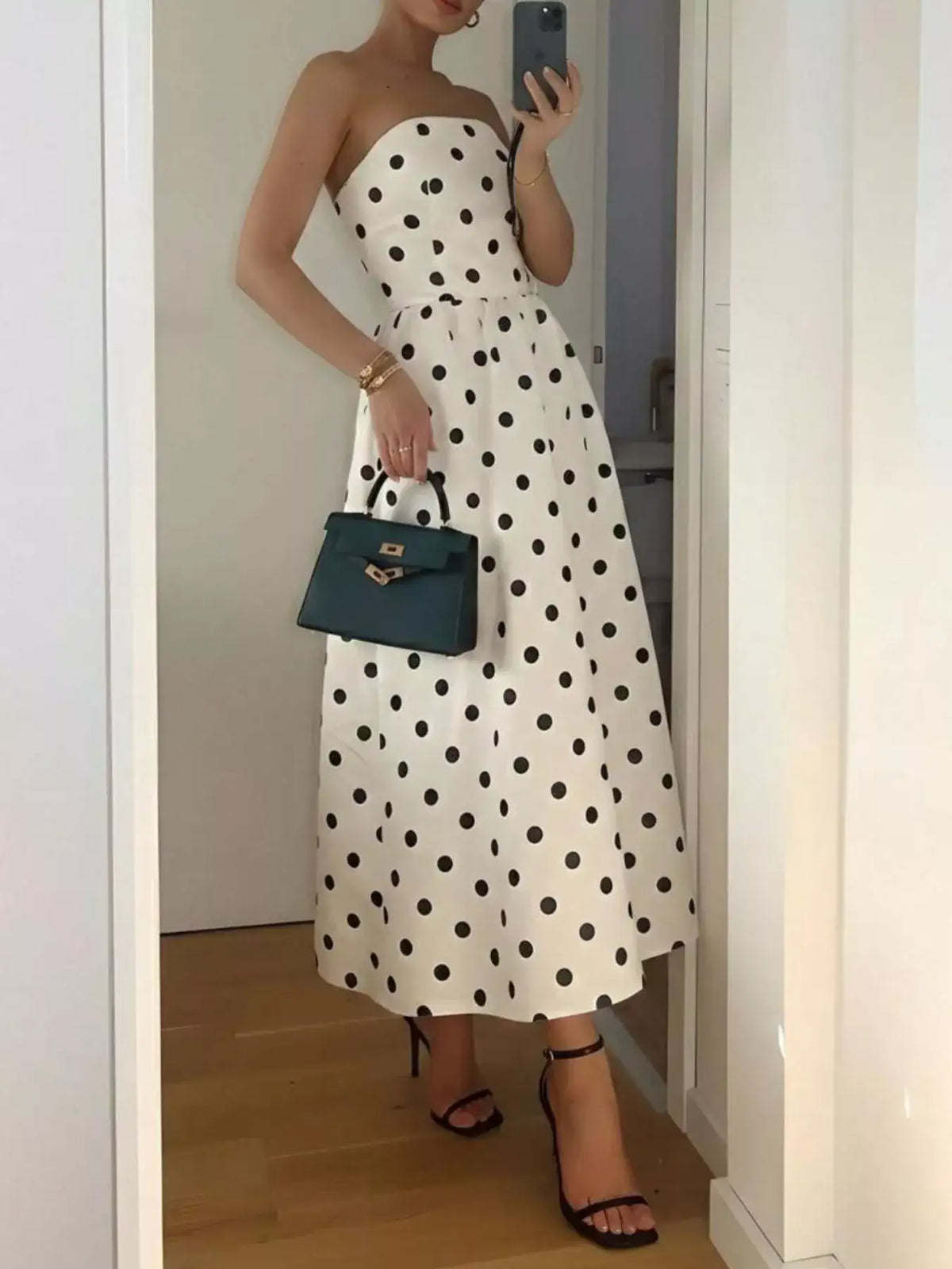 Evie's Dreamland white strapless midi dress with black polka dots, styled with a dark green handbag.