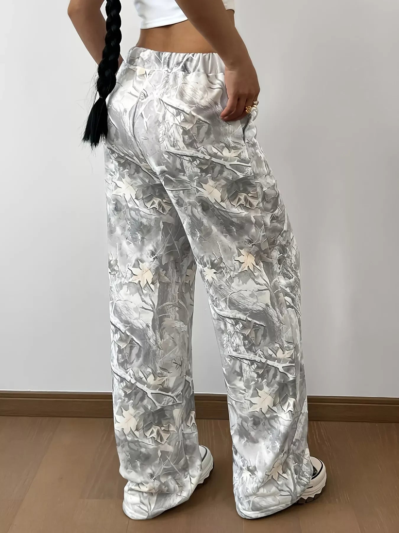 Woman wearing loose gray and white leaf print pants with white platform sneakers on wood floor