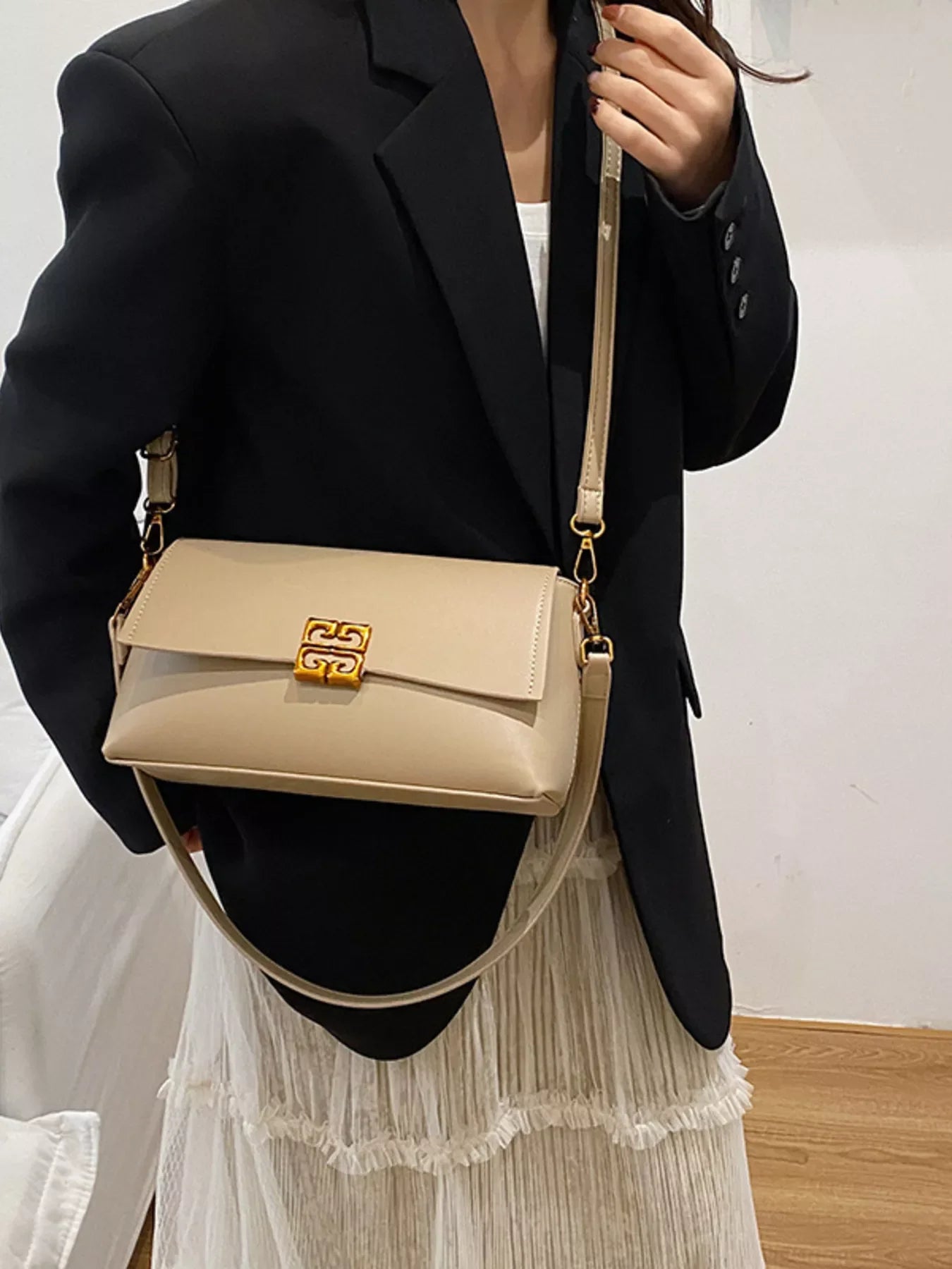 Woman wearing black blazer and pleated white skirt holding beige leather shoulder bag with gold clasp