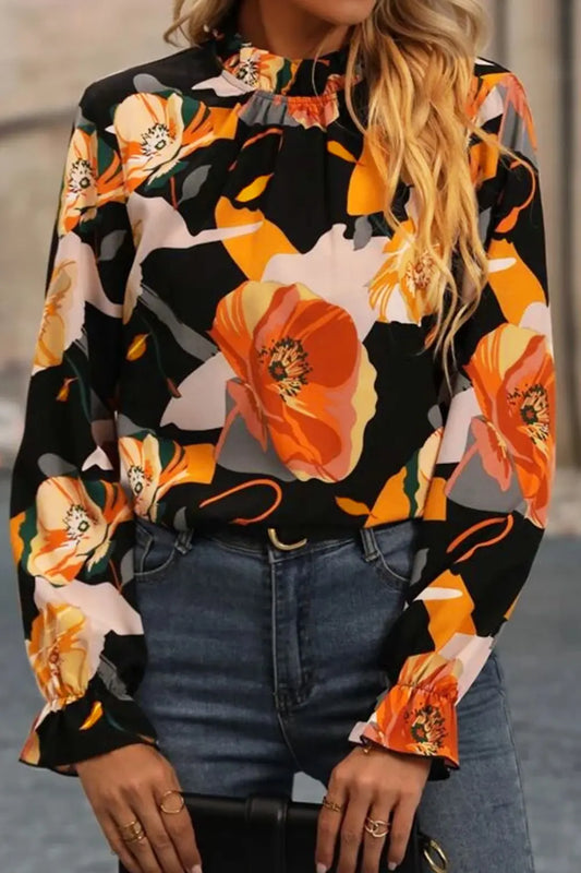 Woman wearing a black floral blouse with large orange and yellow flowers paired with blue jeans