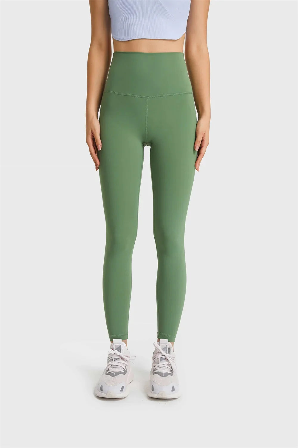 Woman wearing green high-waist leggings and white sneakers on gray background
