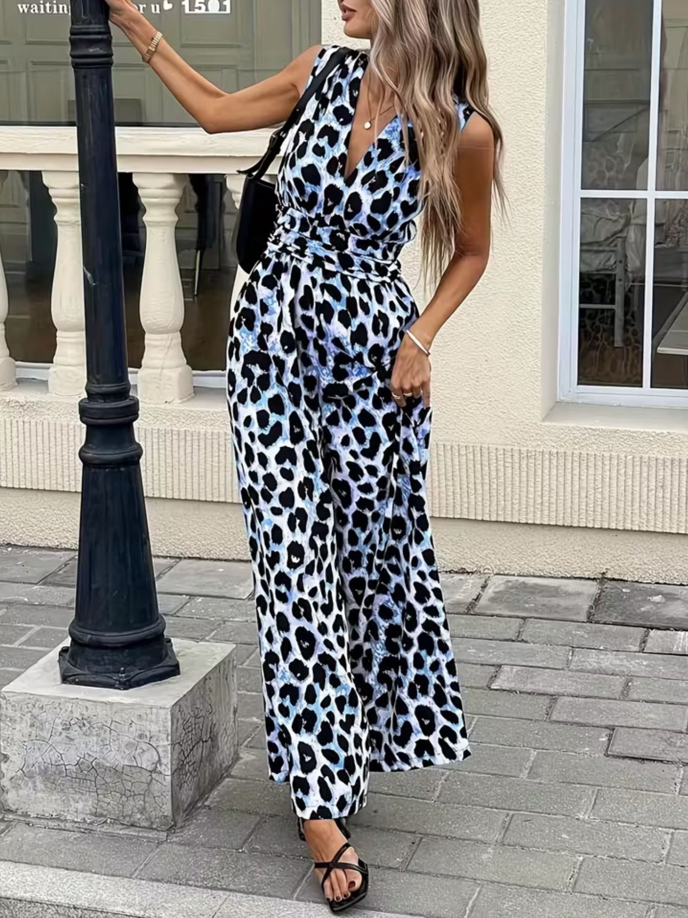 Woman wearing sleeveless blue leopard print jumpsuit and sandals outdoors