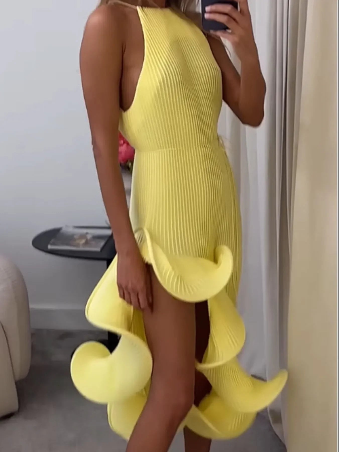 Woman wearing a sleeveless yellow ruffle dress with sculpted high slit detail