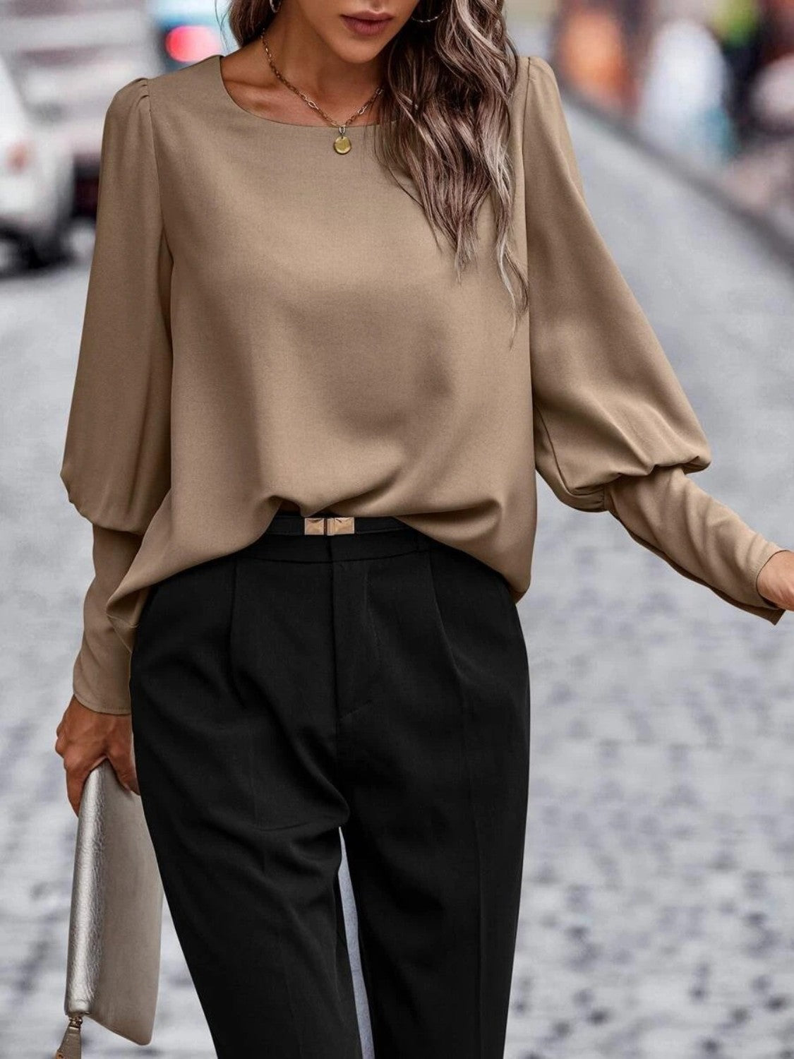 Woman wearing a beige long sleeve blouse with black high-waisted trousers, holding a clutch