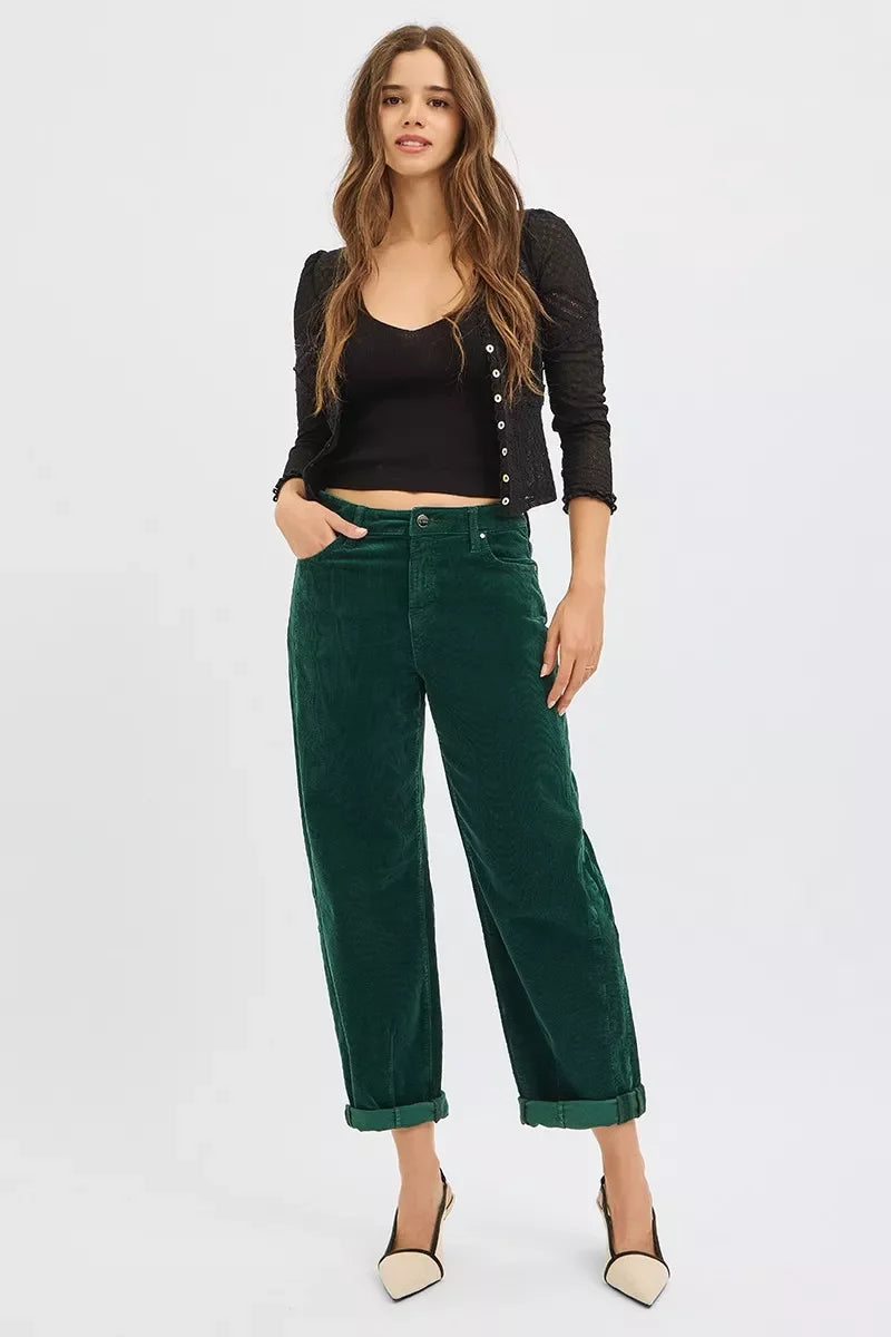 Woman wearing black cropped top, black buttoned cardigan, green rolled-up pants, and beige heels