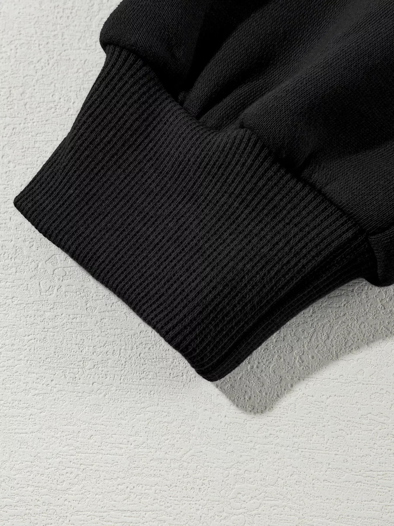 Close-up of black ribbed knit cuff on a black long sleeve garment on textured surface
