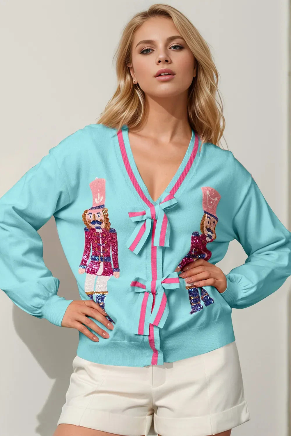 Blonde woman wearing a light blue cardigan with pink bows and sequin nutcracker designs paired with white shorts