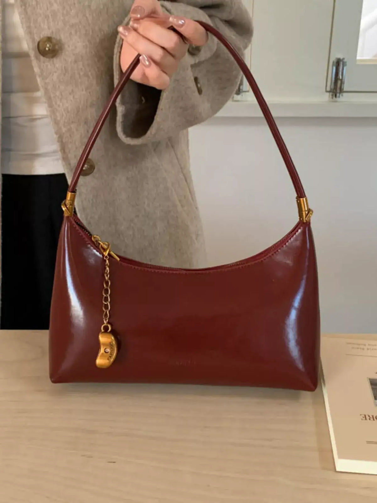 Evie's Dreamland deep red PU leather shoulder bag with a gold chain charm, held by a woman in a beige coat.