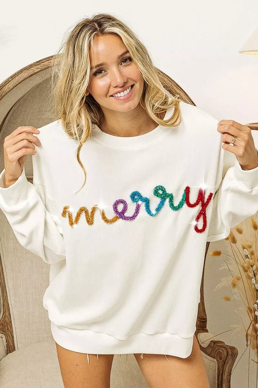 Smiling woman wearing white sweater with colorful glittery merry text sitting on beige chair