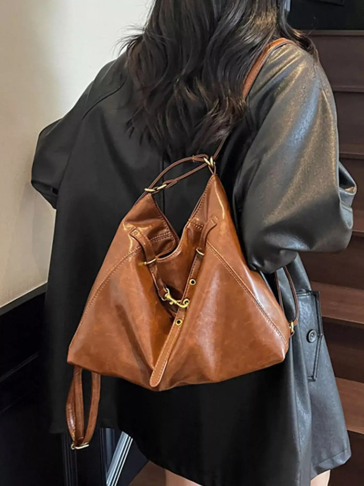 Back view of a woman wearing a black faux leather jacket and a brown vintage style PU leather shoulder bag.