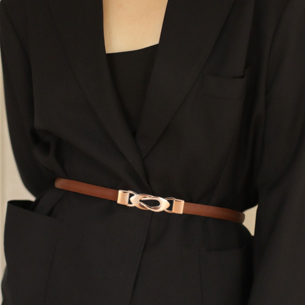 Brown thin leather belt with a gold buckle worn over a black blazer