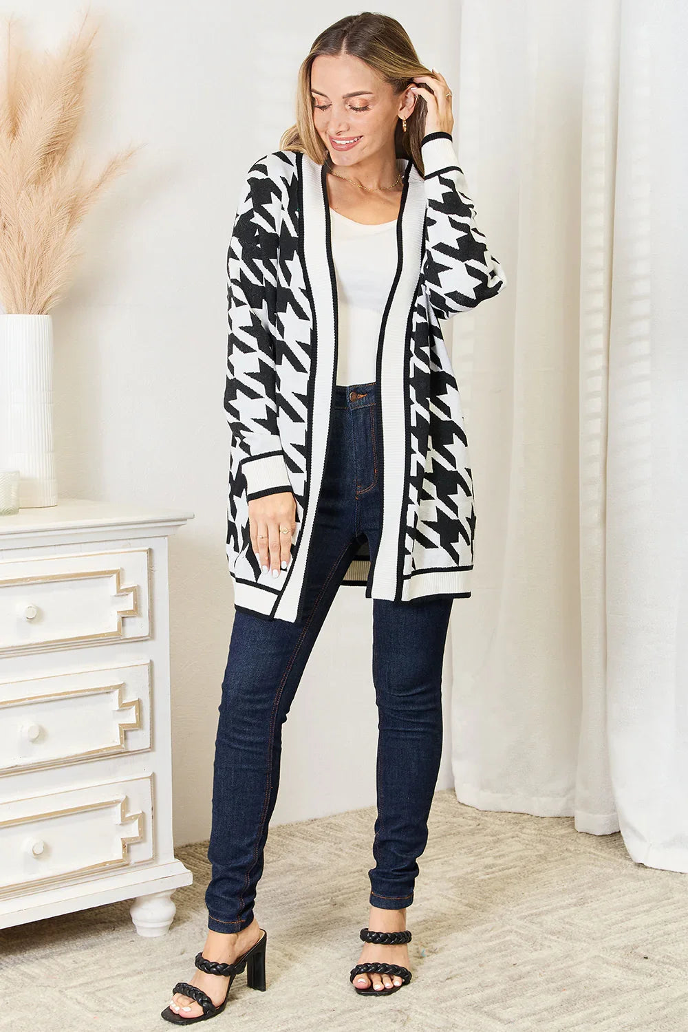 Woman wearing black and white houndstooth cardigan, white top, dark skinny jeans, and black heeled sandals