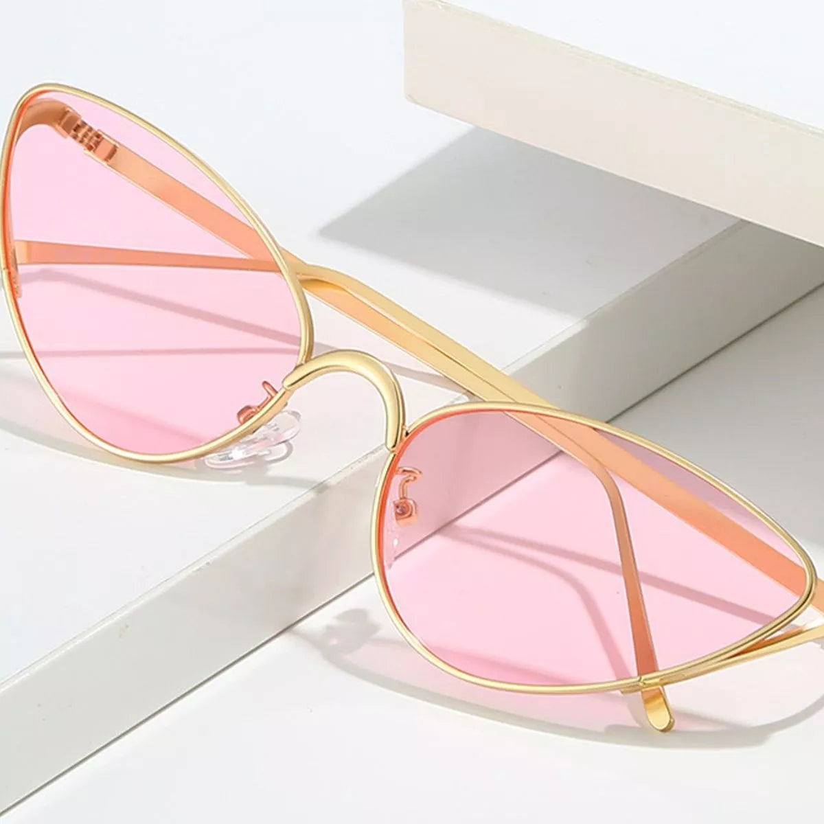Gold-framed sunglasses with pink tinted lenses resting on a white surface