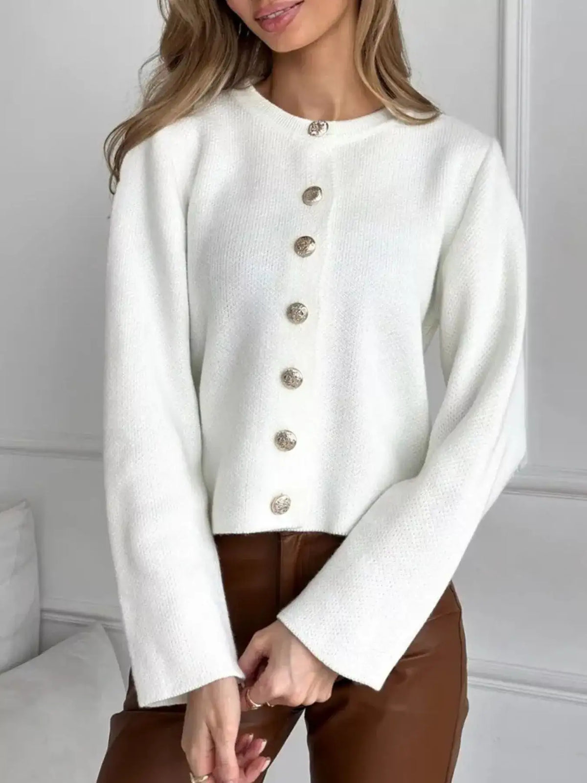 Woman wearing a white crew neck button down cardigan by Evie's Dreamland paired with brown leather pants.