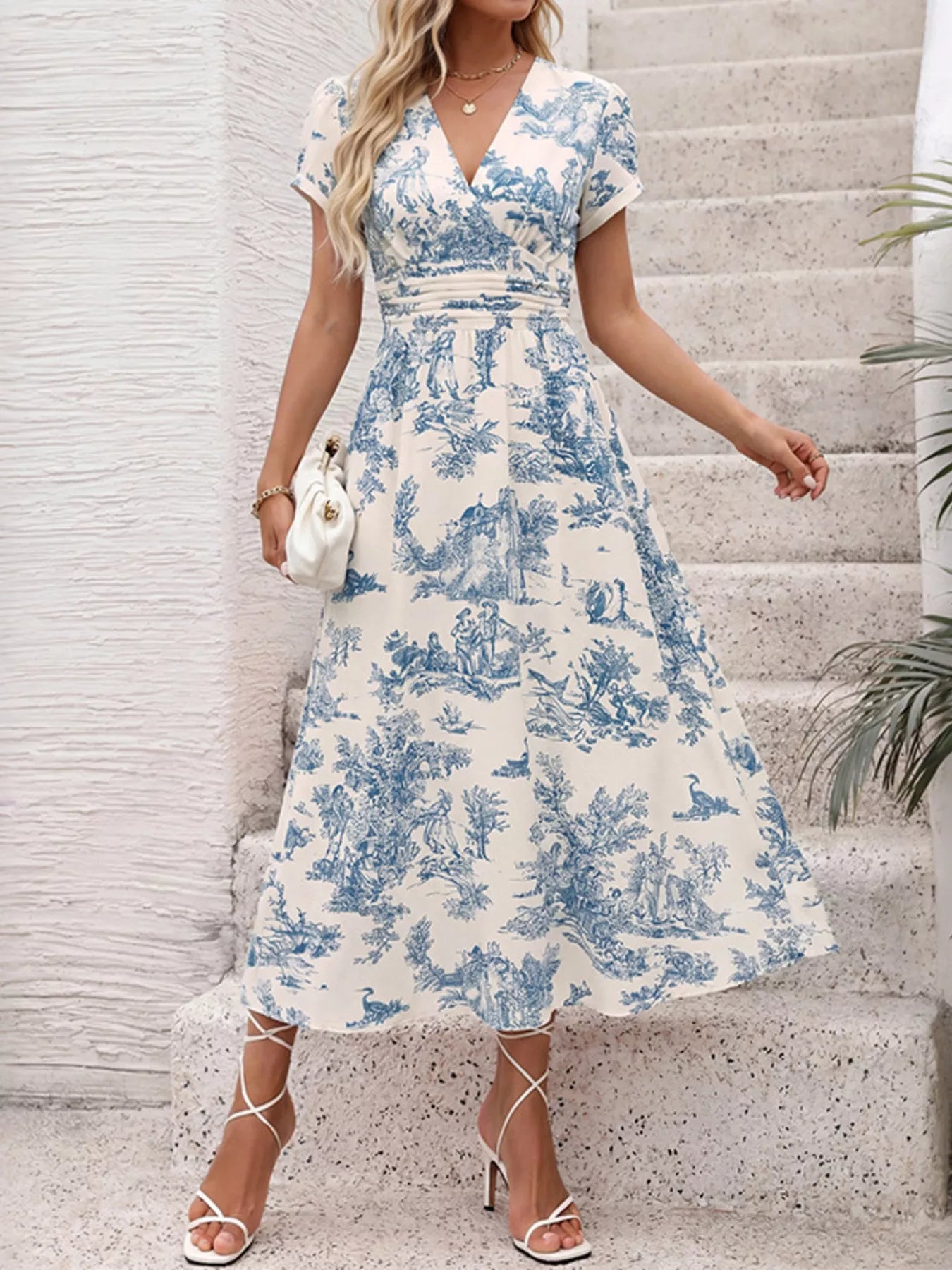 Blue and white toile print midi dress with V-neck, puff sleeves, and cinched waist, styled with white heels and clutch.