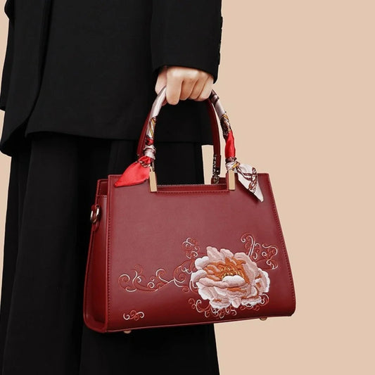 Woman holding elegant red handbag with floral embroidery and scarf-wrapped handles