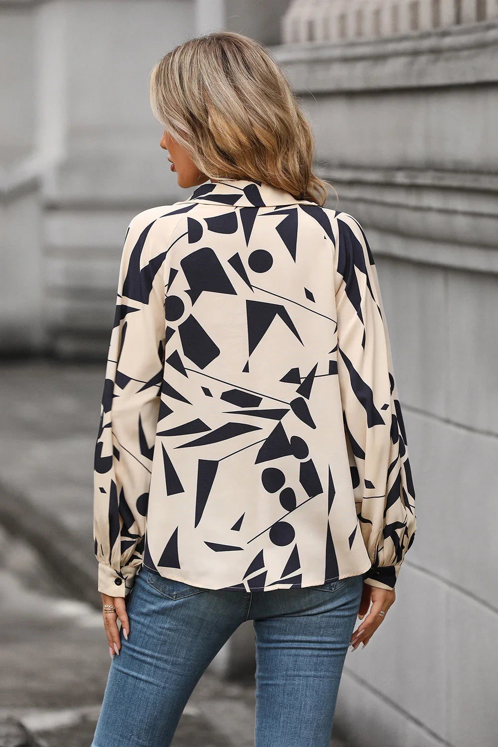 Woman in beige and black geometric print blouse with long sleeves, styled with blue jeans