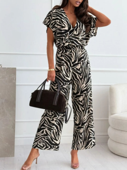 Woman wearing black and white zebra print jumpsuit with black handbag in modern interior