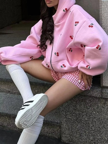 Woman wearing pink cherry print hoodie, pink gingham shorts, white knee-high socks, and white sneakers sitting on stone steps