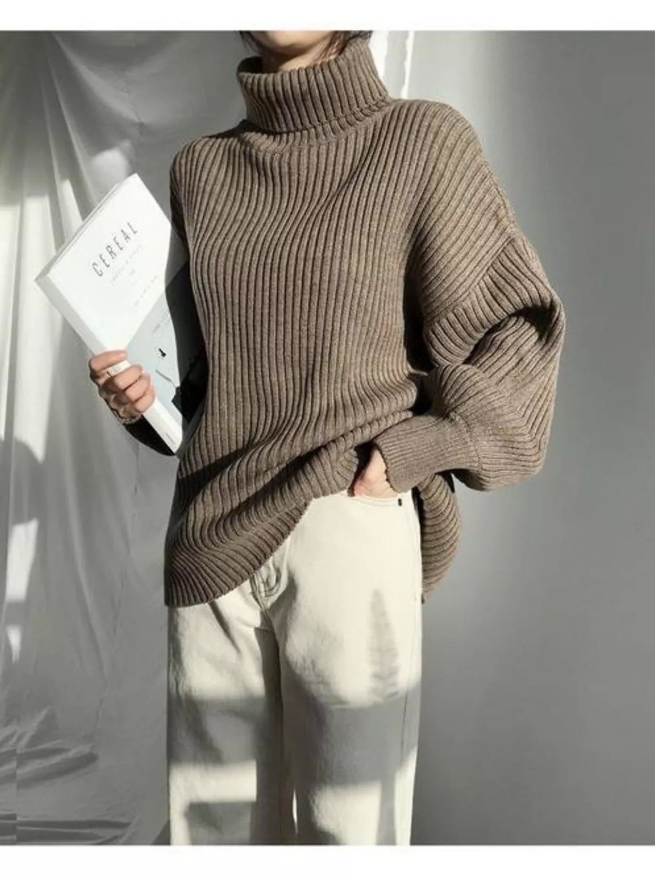 Woman wearing a brown oversized ribbed turtleneck sweater and white trousers