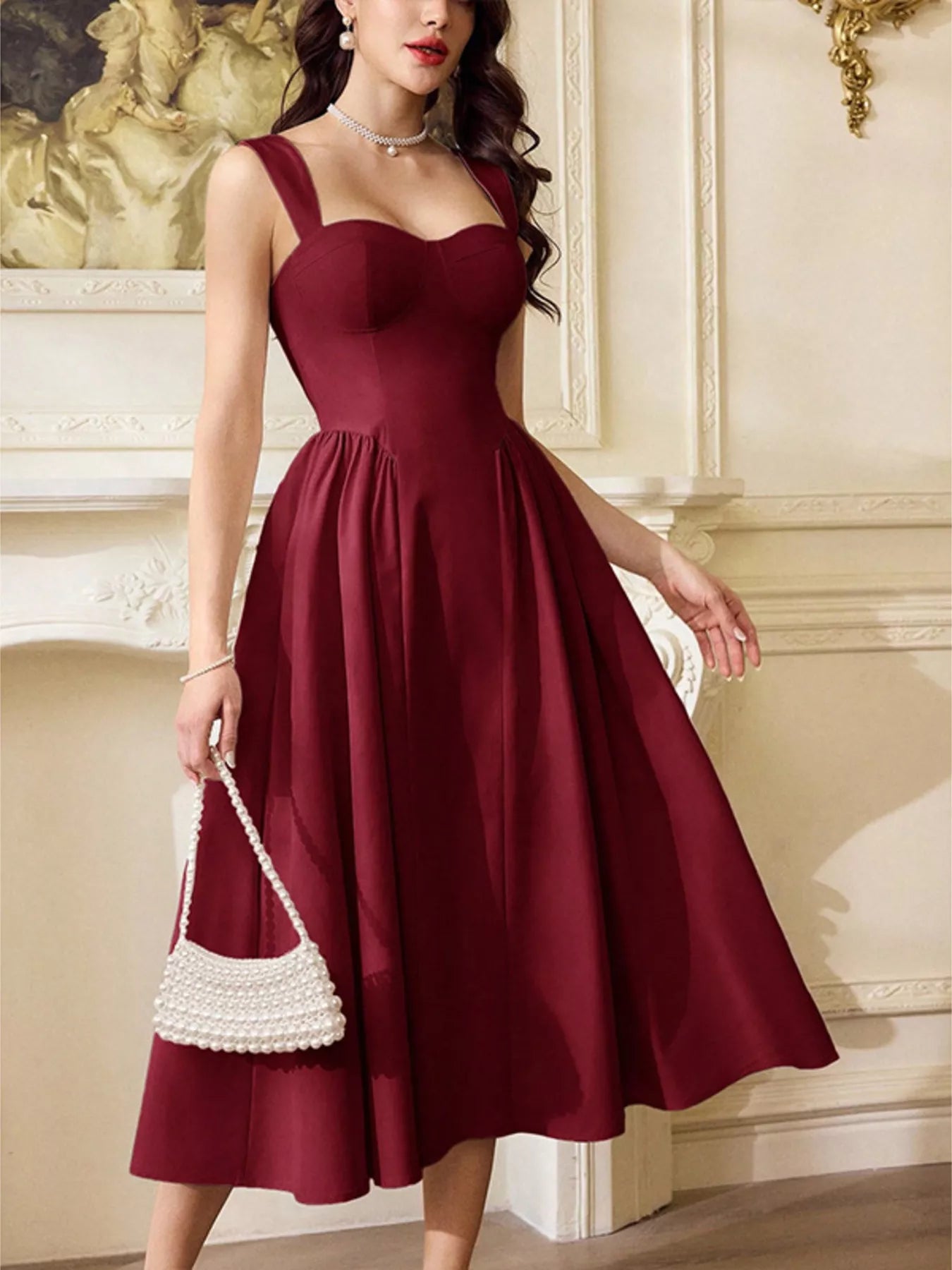 Woman wearing a burgundy sleeveless A-line midi dress and holding a white pearl handbag.