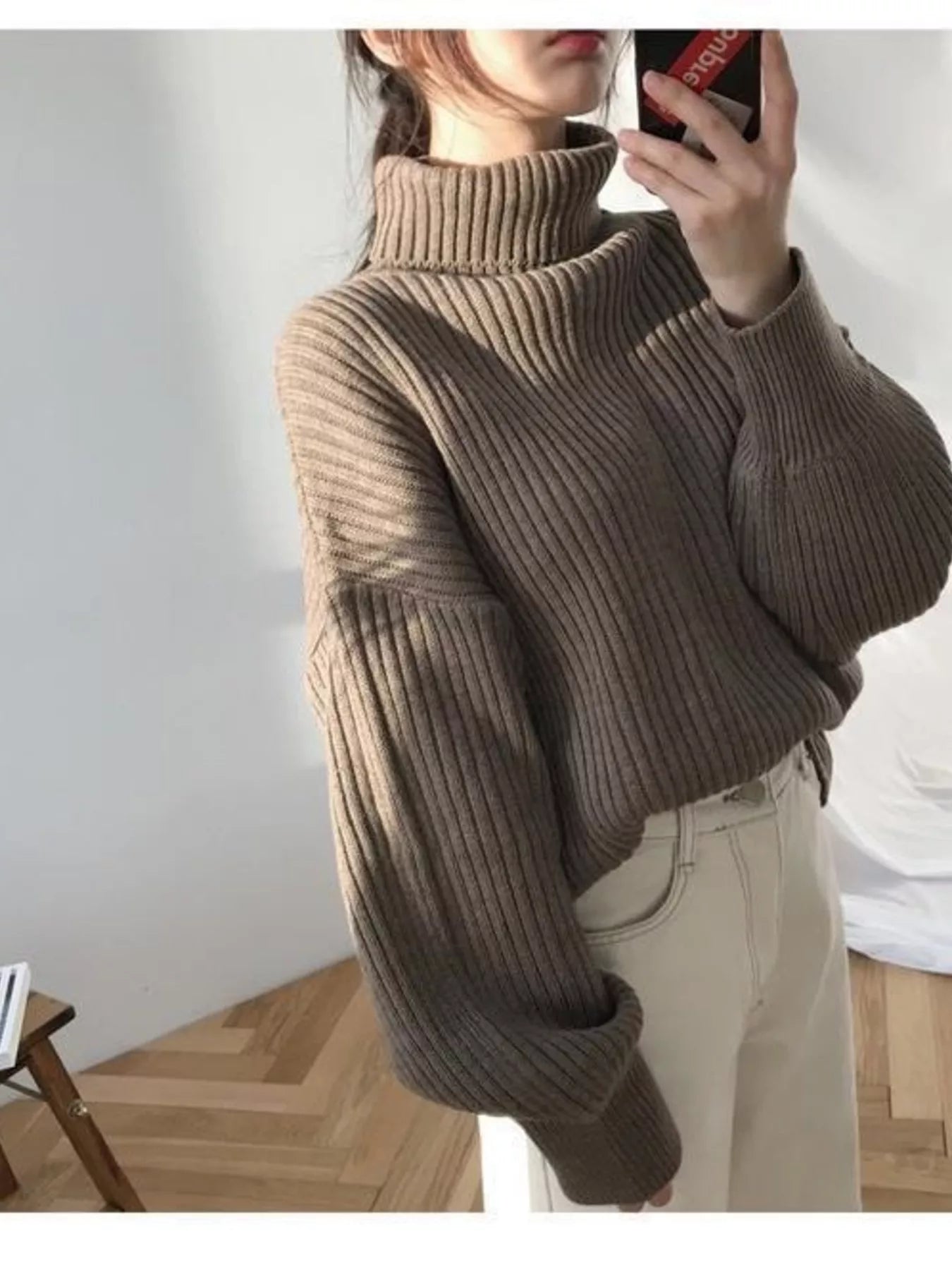 Woman wearing an oversized brown ribbed turtleneck sweater and white trousers