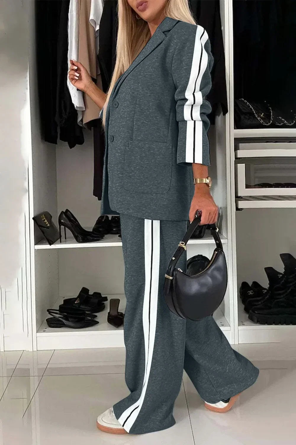 Woman in grey athleisure suit with white stripes, holding black handbag in stylish closet