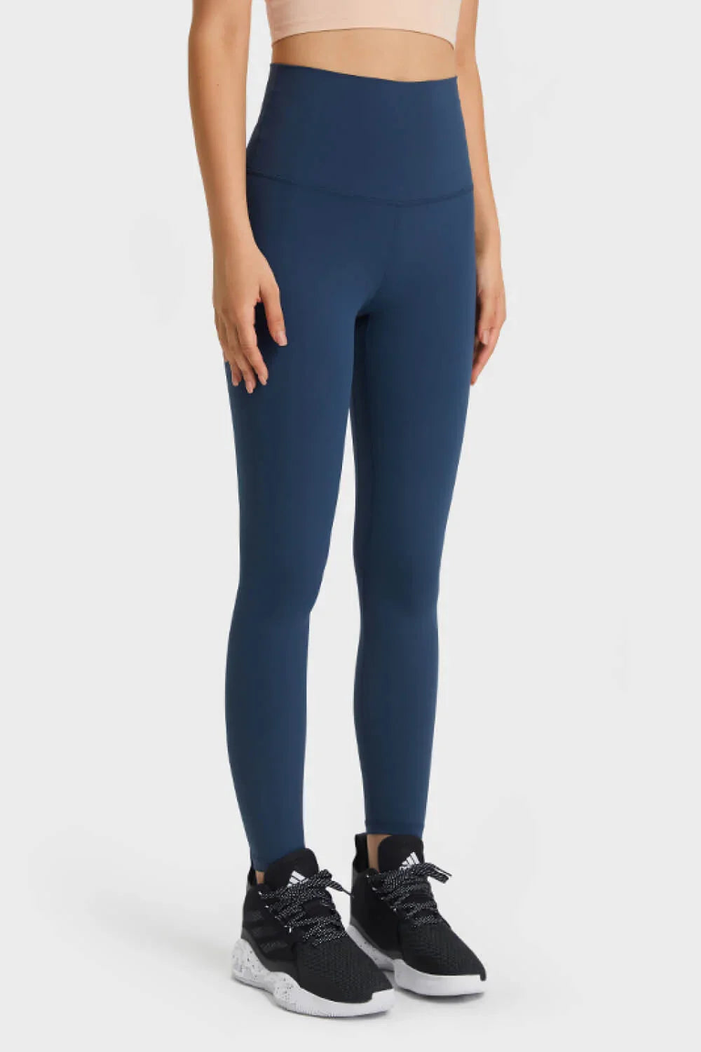 Woman wearing navy blue high-waisted leggings and black athletic sneakers on white background