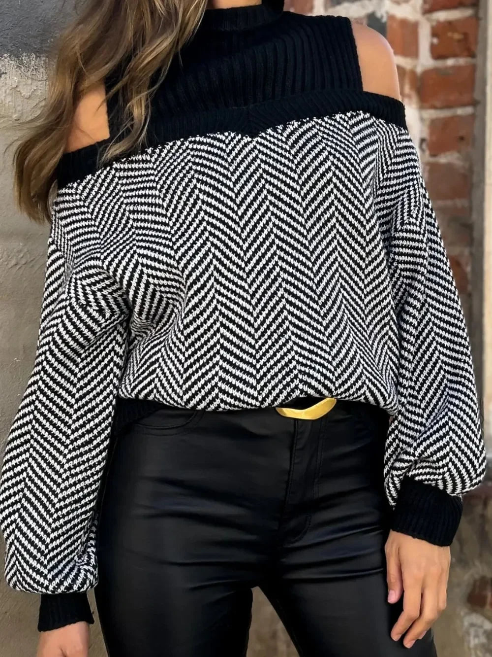 Woman wearing black and white herringbone cold shoulder sweater with black high-waisted pants and gold buckle belt