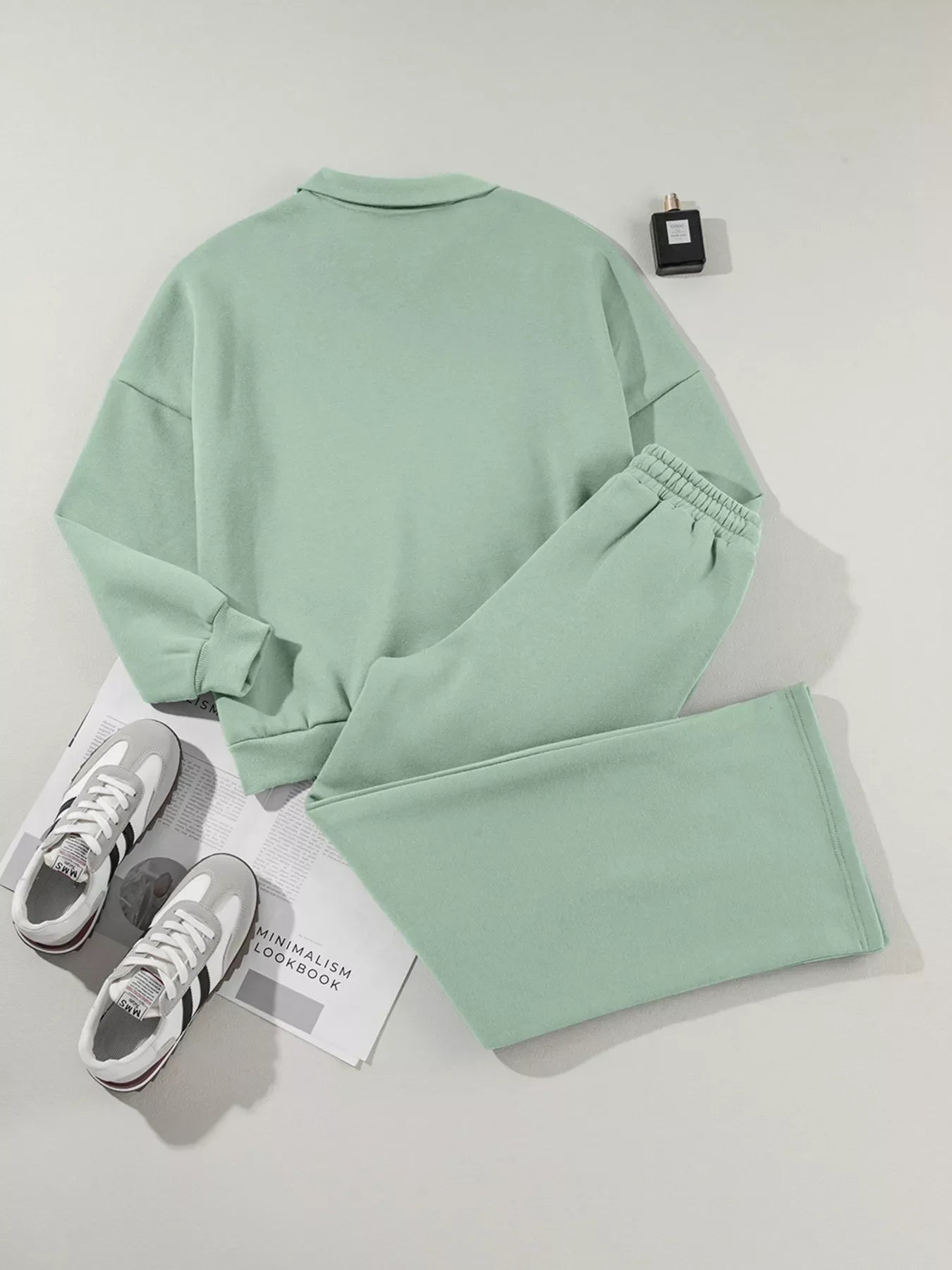 Mint green casual sweat suit with elastic waist pants and crewneck sweatshirt, paired with gray and white sneakers and black perfume bottle