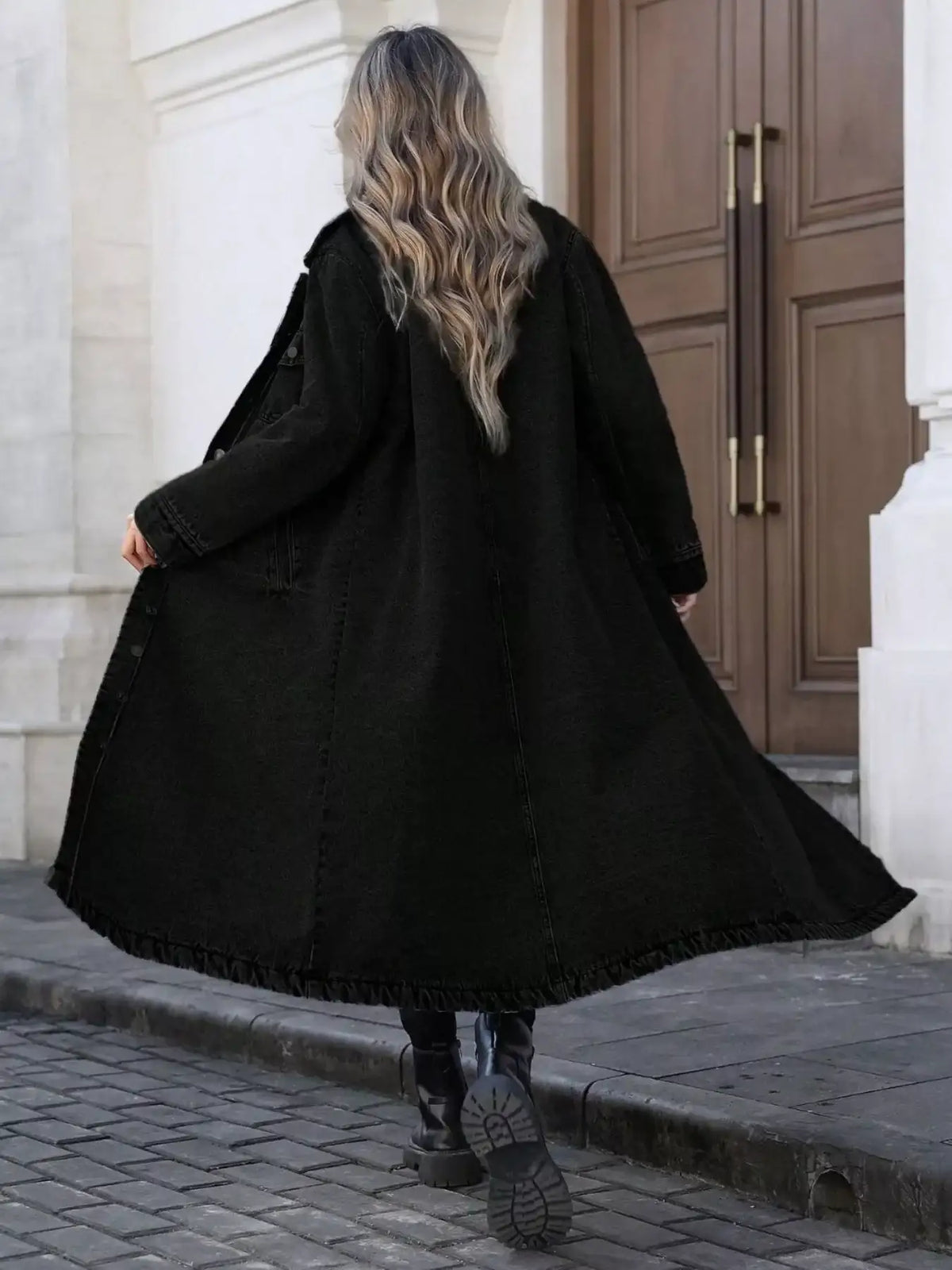 Back view of a woman wearing a black longline denim jacket by Evie's Dreamland with black boots.