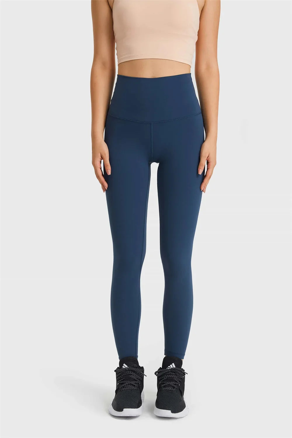 Woman wearing navy high-waisted leggings and black athletic shoes on white background