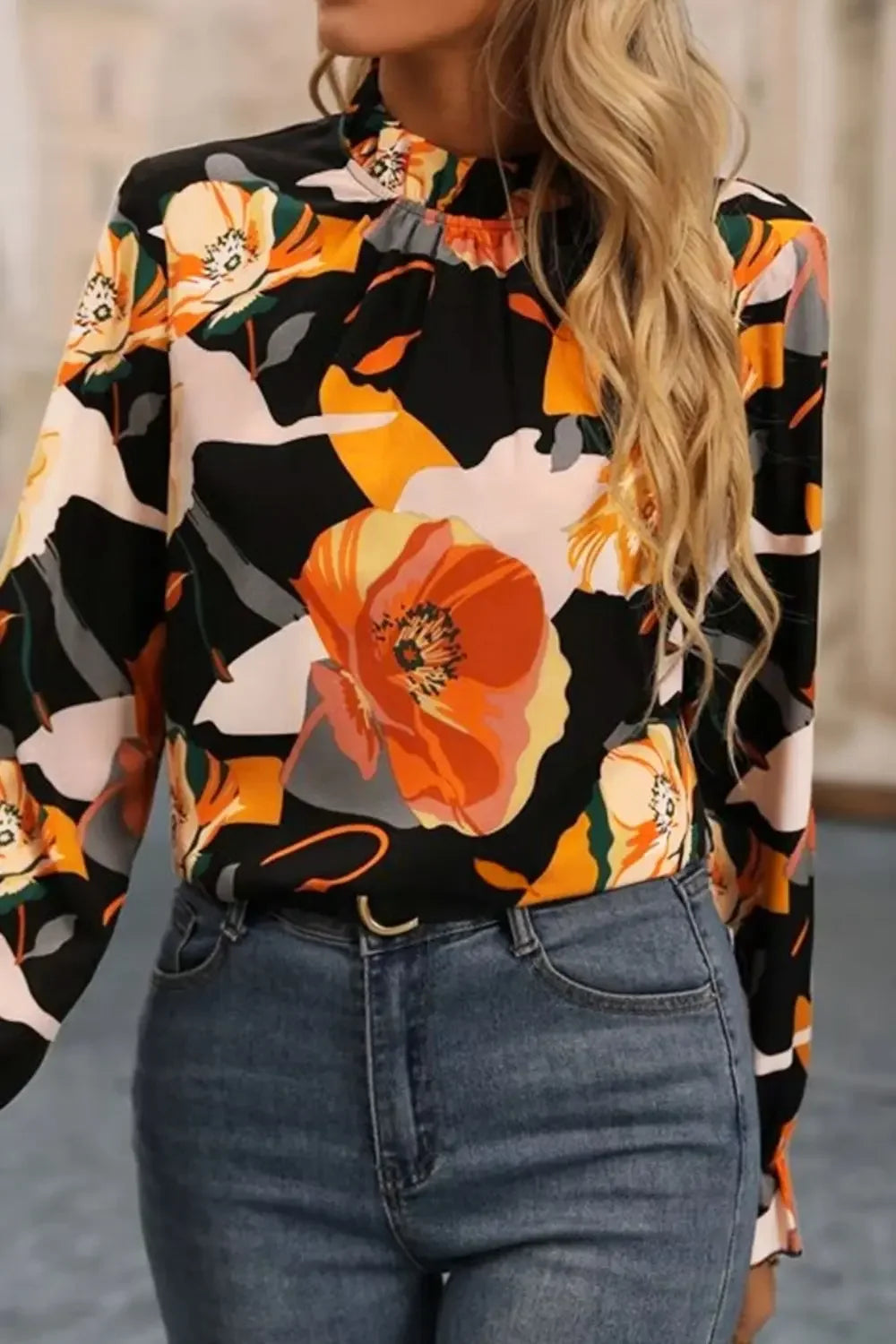 Woman wearing black floral print blouse with orange and yellow flowers paired with blue jeans