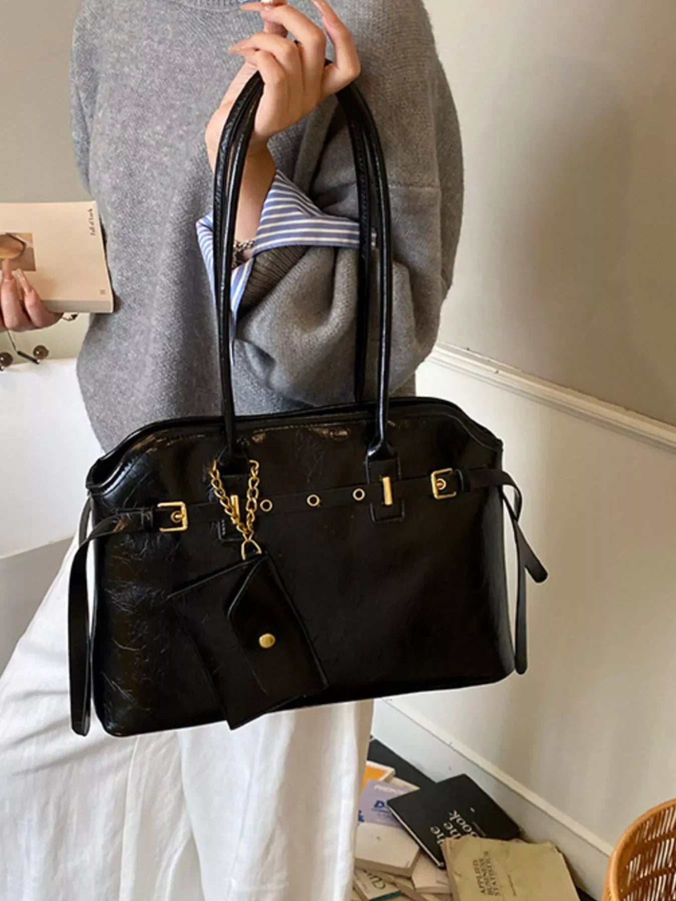 woman holding black leather handbag with gold accents and attached small pouch indoors