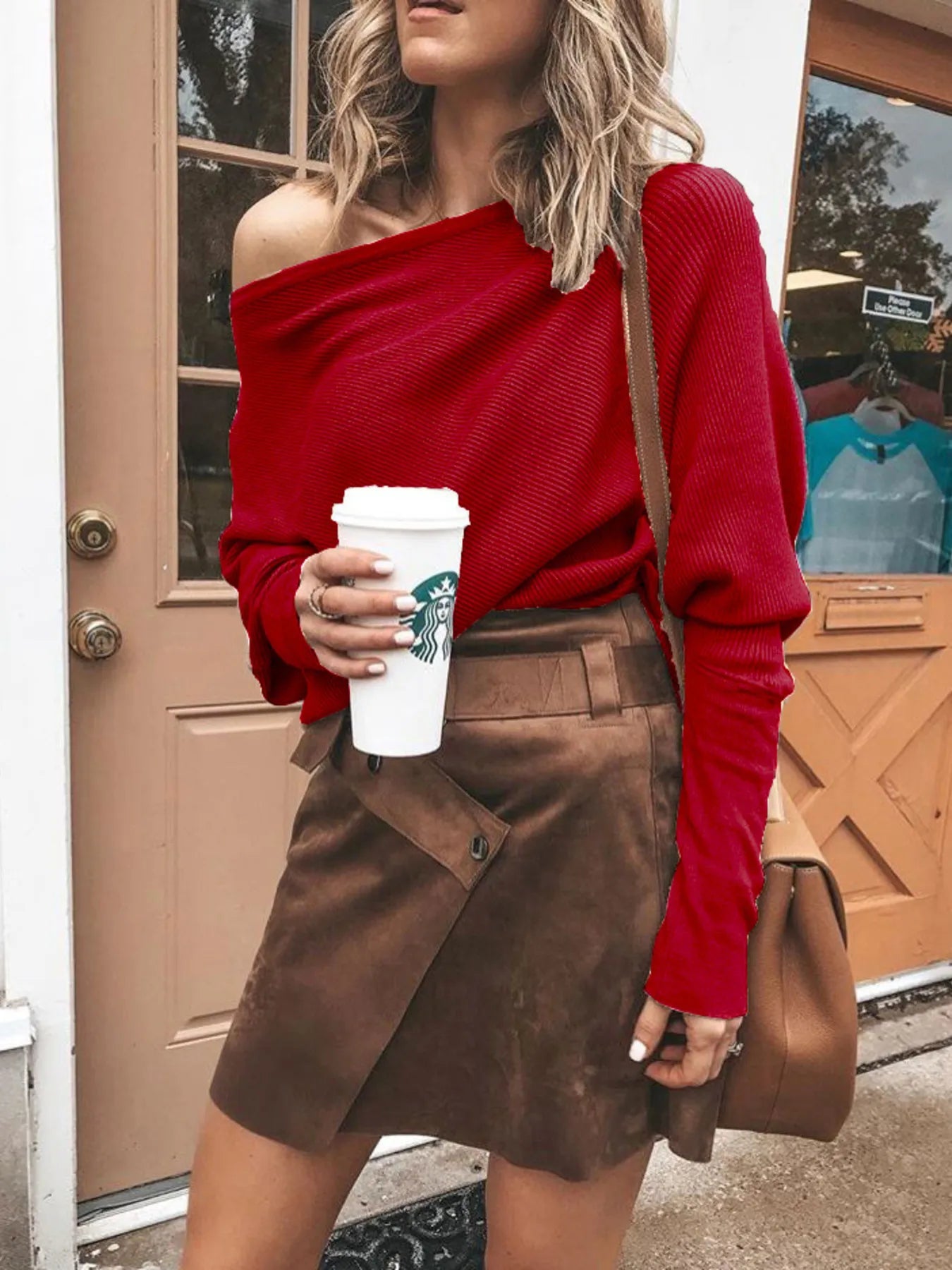 Woman in off-shoulder red sweater and brown suede skirt holding Starbucks coffee cup outdoors