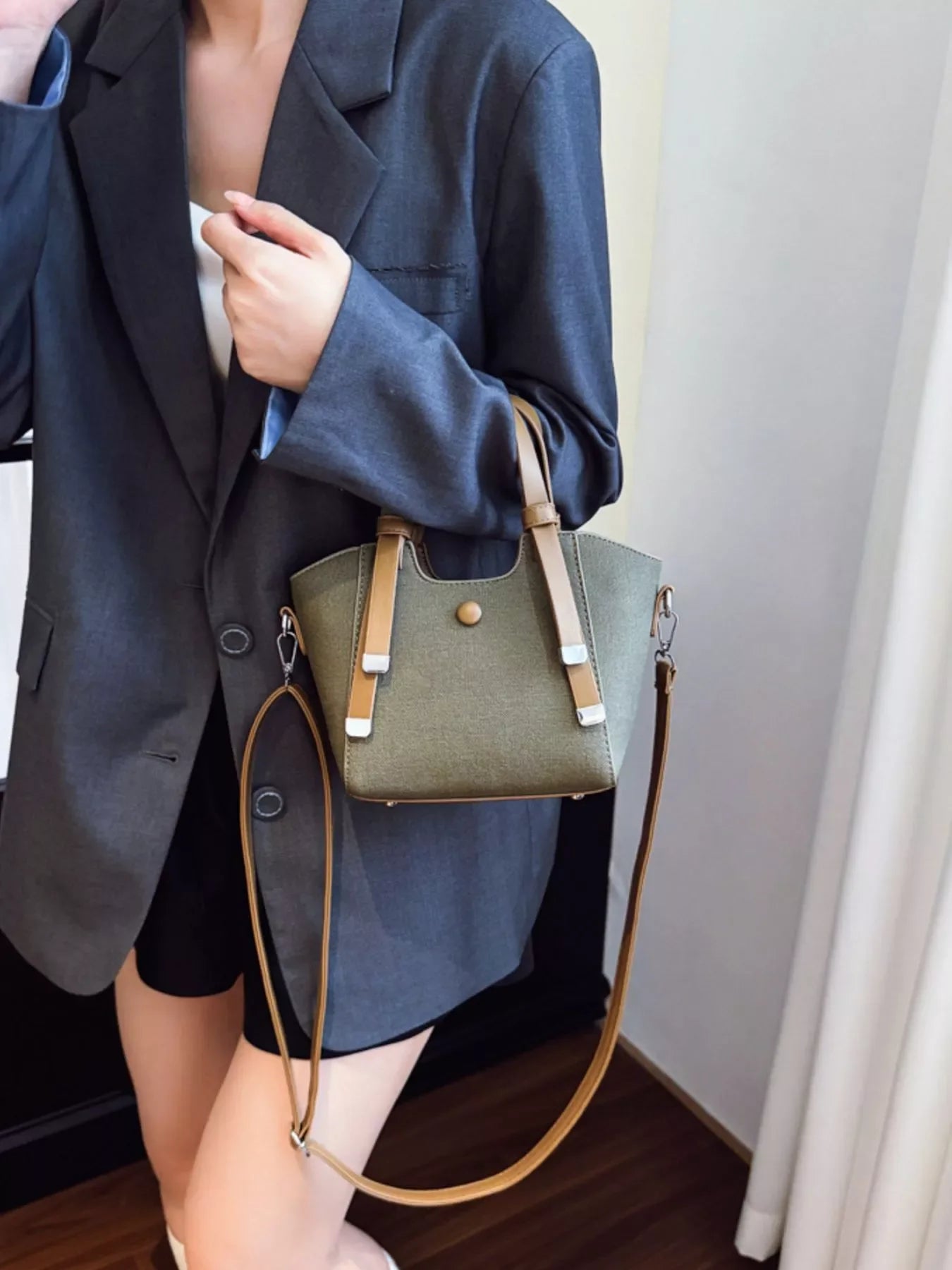 Woman wearing gray blazer holding olive green handbag with brown straps indoors
