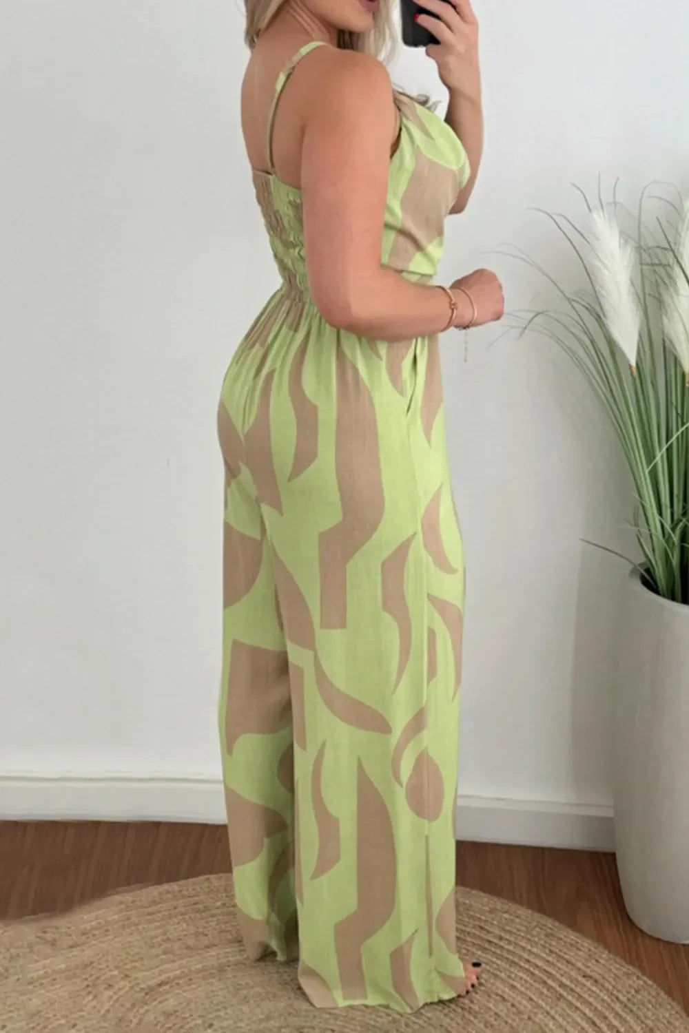 Woman wearing green and beige abstract patterned jumpsuit with spaghetti straps indoors