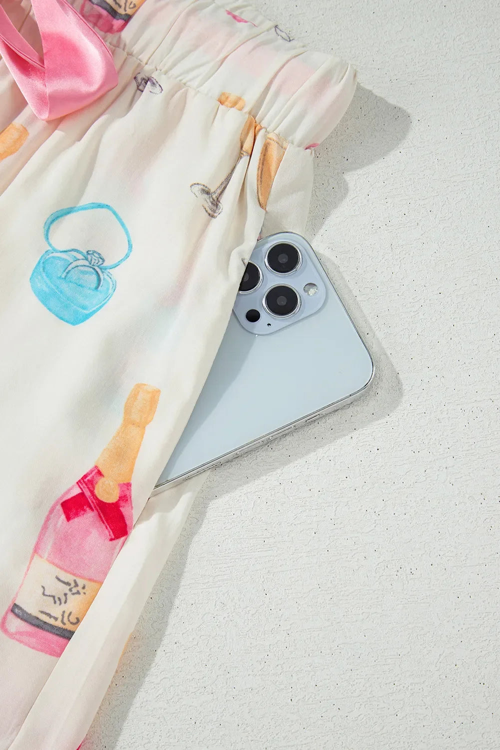 Silver smartphone partially tucked into pocket of white fabric with colorful drink and ring box illustrations