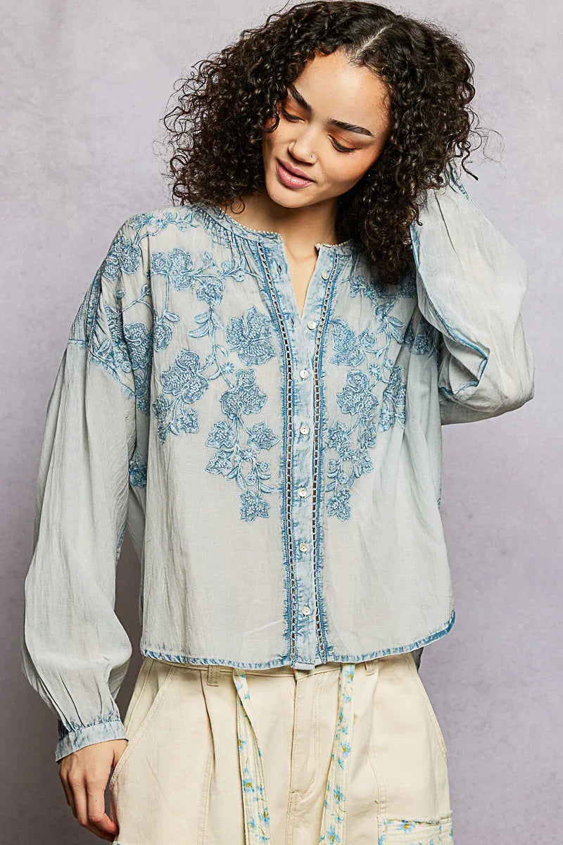 Woman wearing a light blue floral embroidered blouse with button front and long sleeves