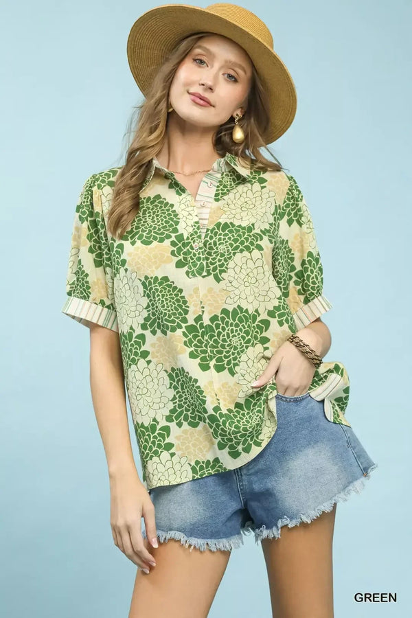 Woman in green floral short sleeve blouse, denim shorts, and straw hat on light blue background