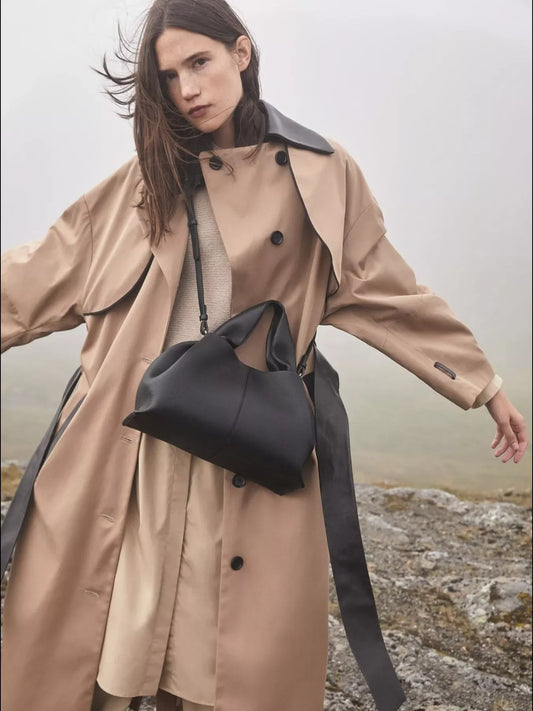 Woman in beige trench coat with black collar and black leather handbag in foggy outdoor setting