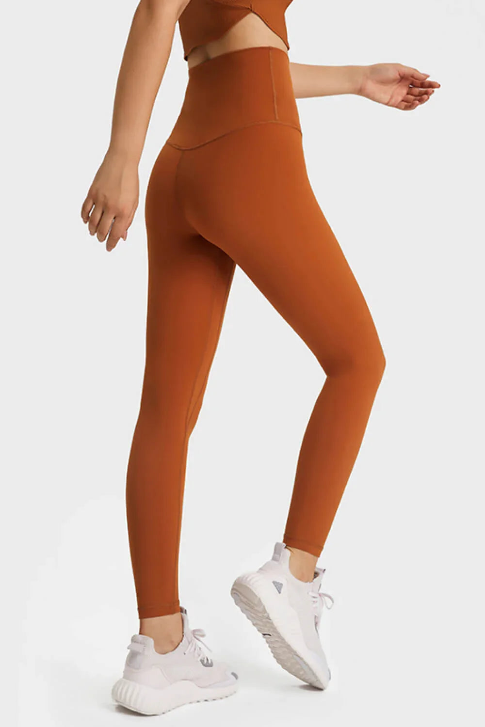 Woman wearing rust-colored high-waisted leggings and white sneakers on white background