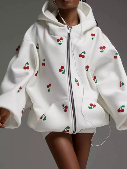 White zip-up hoodie with red cherry print and oversized sleeves worn by person with earbuds