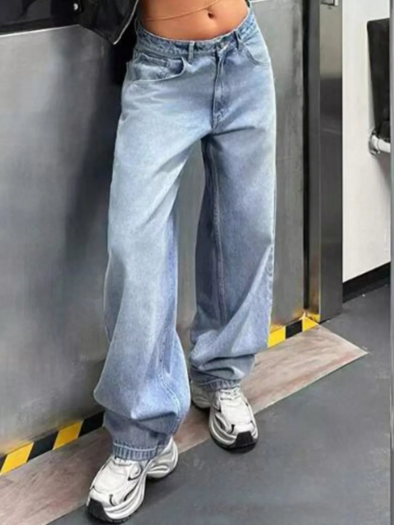 Woman wearing high-waisted baggy light wash jeans with white sneakers in urban setting