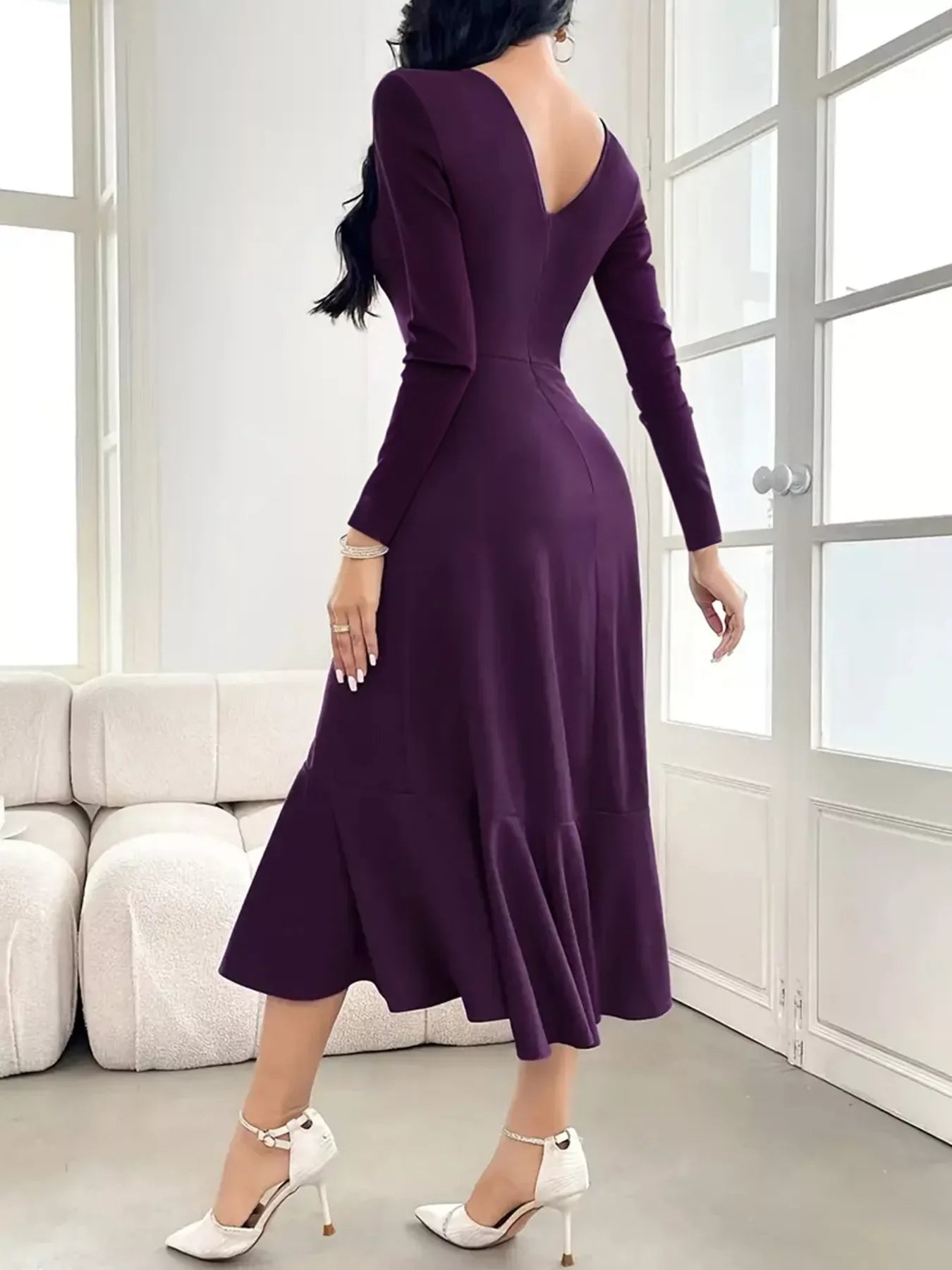 Woman wearing a fitted long-sleeve purple midi dress with deep V back and white high heels indoors