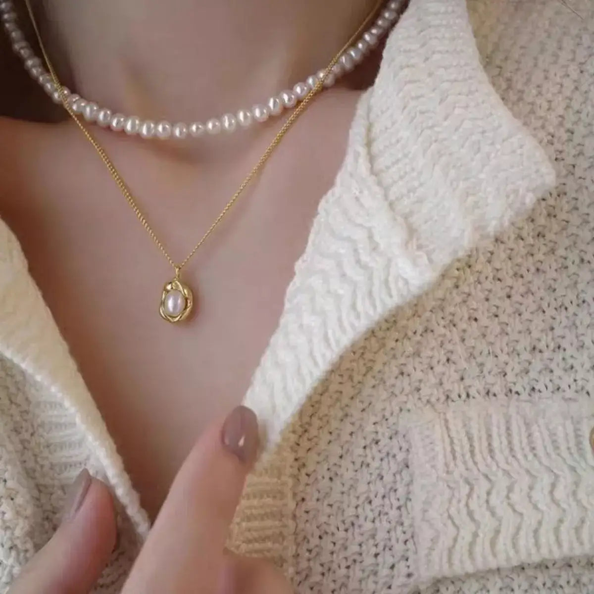 Layered Evie's Dreamland freshwater pearl necklaces with a gold pendant over a cream knit top.