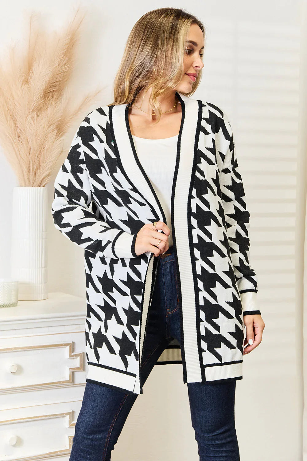 Woman wearing black and white houndstooth cardigan over white top and blue jeans in bright indoor setting